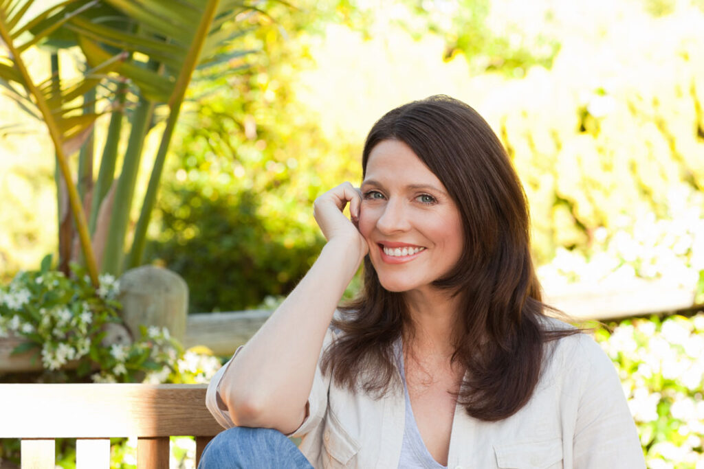 Mulher olhando para o espelho com um sorriso confiante, simbolizando autoestima e autovalorização.